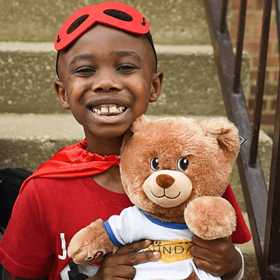 child in cape and mask hugging bear